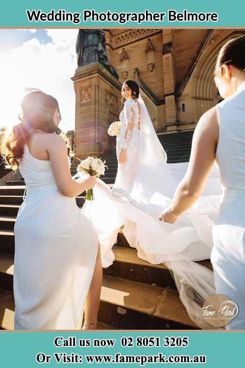 Photo of the Bride smiling on the bridesmaid holding the tail of her wedding gown at the front of the church Belmore NSW 2192