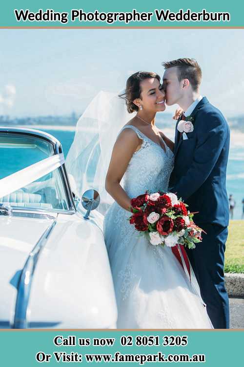 Photo of the Groom kiss the Bride besides the bridal car Wedderburn NSW 2560